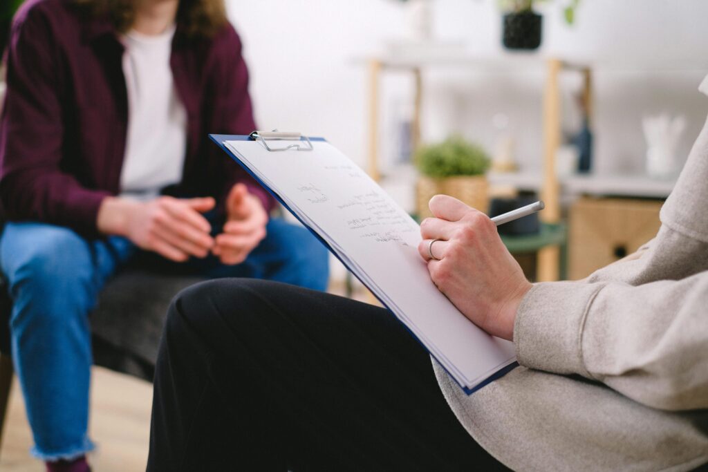 Person with a clipboard with another person sitting in the background
